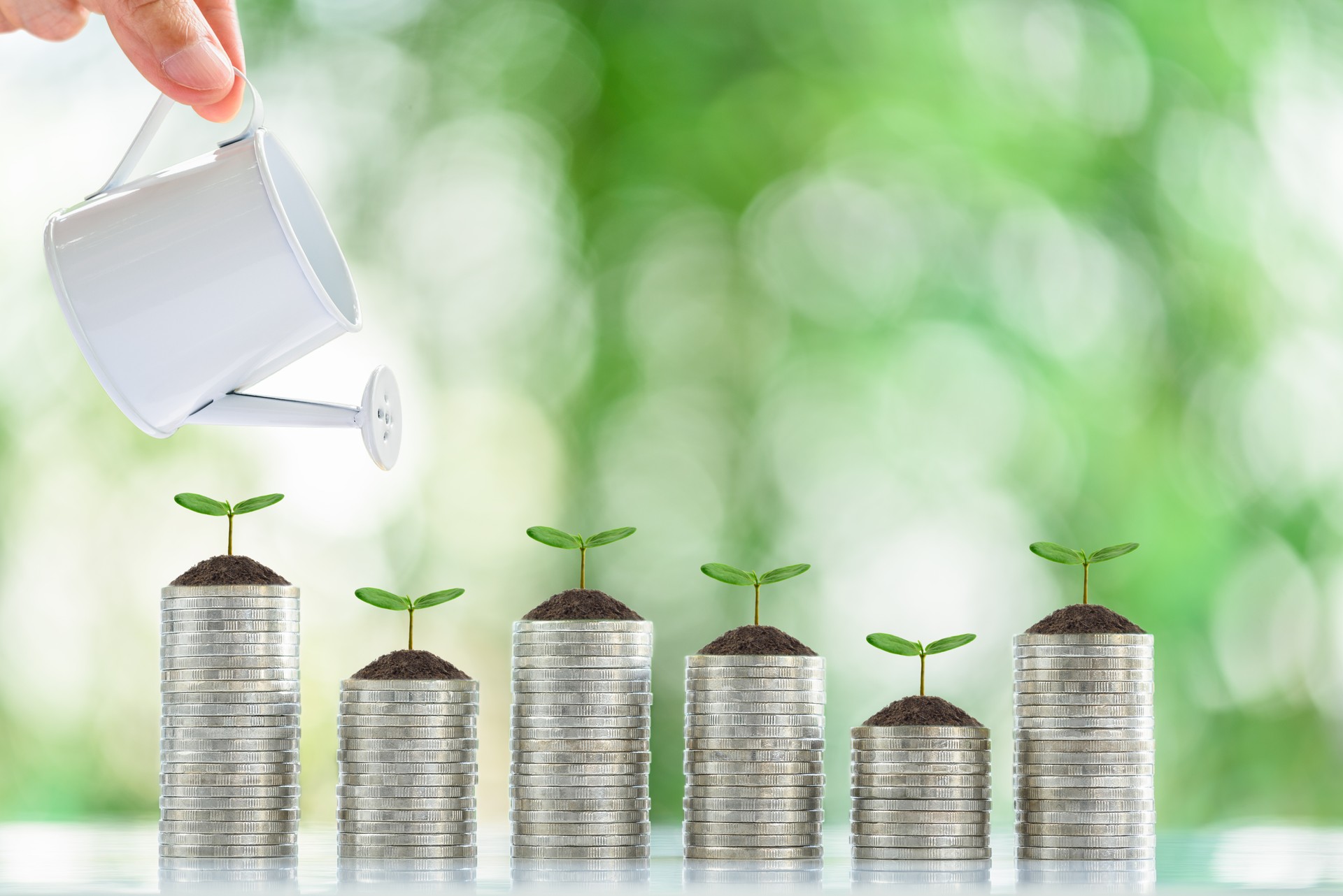 Long-term financial goal setting for most people, financial concept : Hand pours water from a watering can onto a young sprout or a small tree on coin stack, depicting investment increase through time